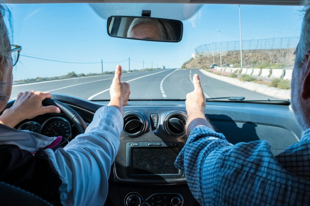 couple of seniors driving and having fun together with a rent car in the street - two pensioners