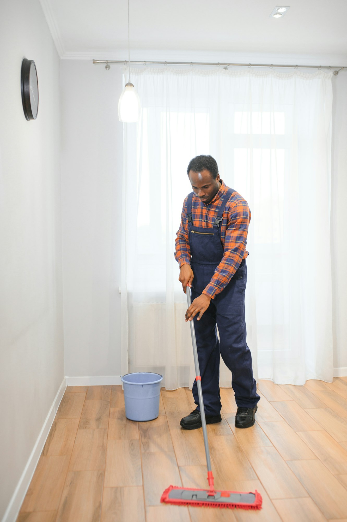 Professional cleaner in blue uniform washing floor and wiping dust from the furniture